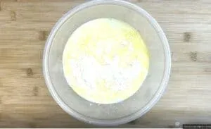 Mixing flour and eggs in a clear bowl on a wooden table, viewed from above.